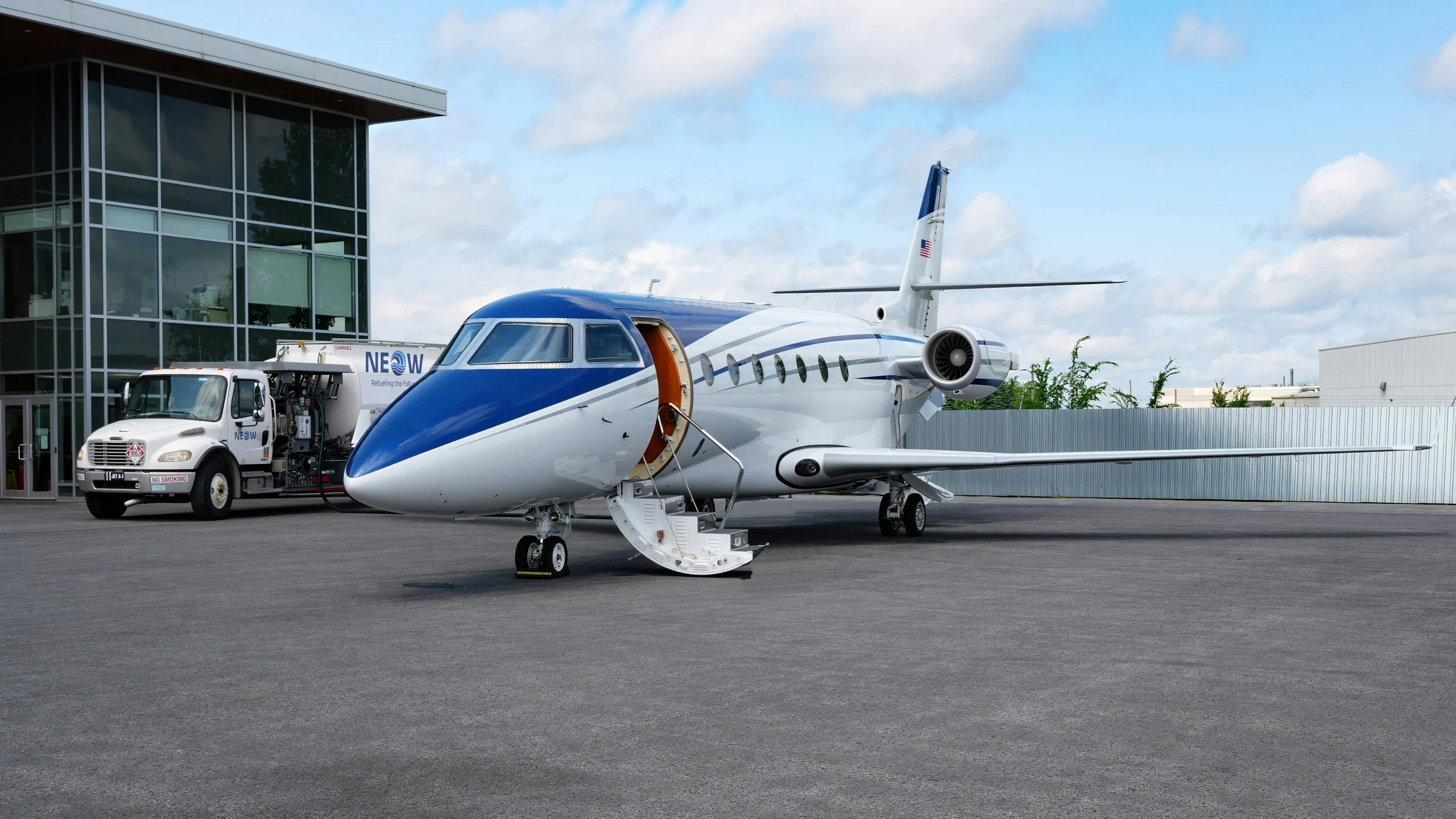 A business jet with its airstair down in front of an airport terminal, a jet fuel tanker truck beside it